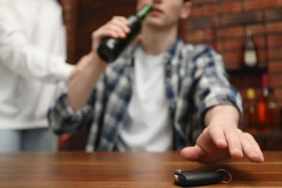 Drunk Driving Statistics, Person drinking a beer bottle while reach for car keys at bar, Disparti Law Group